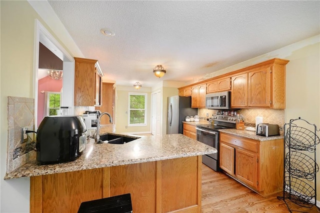kitchen featuring decorative backsplash, a peninsula, a sink, light wood-style flooring, and appliances with stainless steel finishes