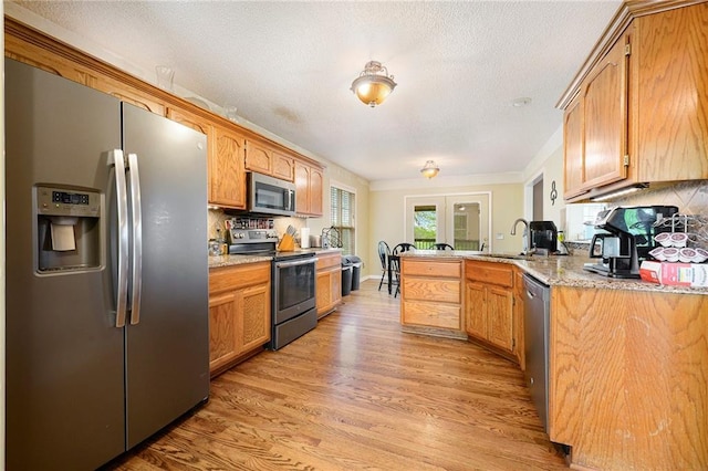 kitchen featuring a peninsula, light wood-type flooring, french doors, a sink, and appliances with stainless steel finishes
