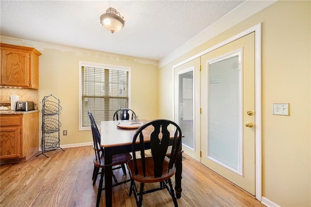 dining area featuring baseboards, a textured ceiling, and light wood-style flooring