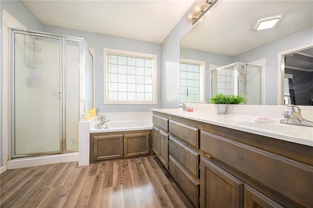 bathroom with double vanity, a garden tub, a stall shower, wood finished floors, and a sink