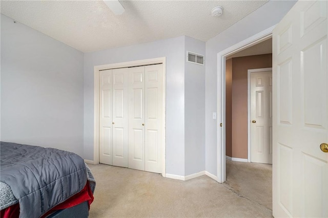 bedroom featuring light carpet, a textured ceiling, baseboards, visible vents, and a closet