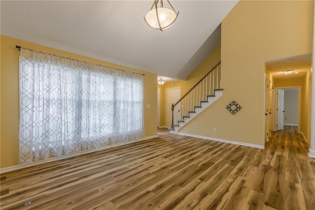 unfurnished living room with stairway, baseboards, vaulted ceiling, and wood finished floors