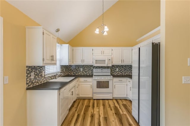kitchen with dark countertops, white appliances, light wood-style floors, a sink, and backsplash