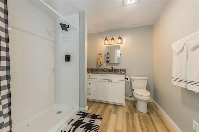 bathroom with a tile shower, wood finished floors, vanity, baseboards, and toilet