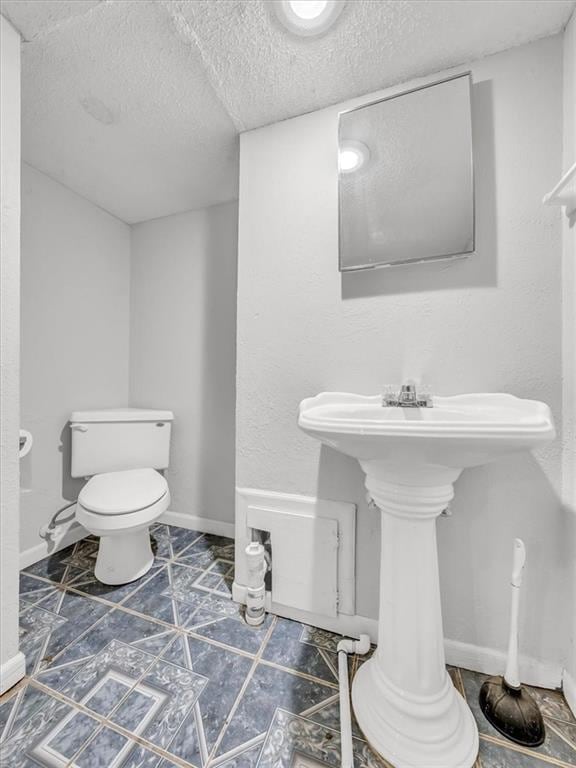 half bath with toilet, a textured ceiling, and baseboards
