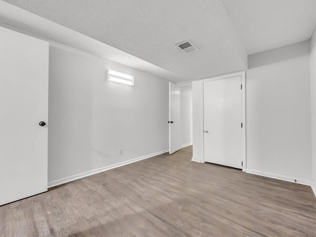 finished basement featuring baseboards, wood finished floors, visible vents, and a textured ceiling