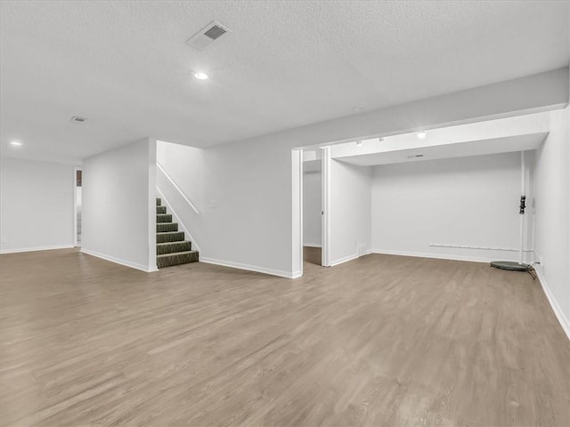 finished basement with stairway, wood finished floors, baseboards, visible vents, and recessed lighting