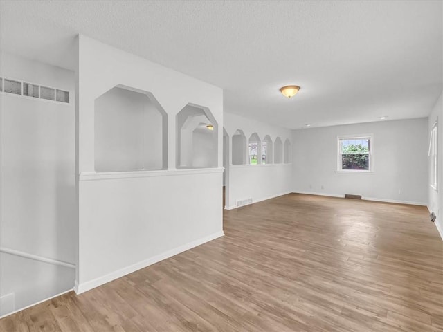 empty room featuring baseboards, wood finished floors, visible vents, and a textured ceiling