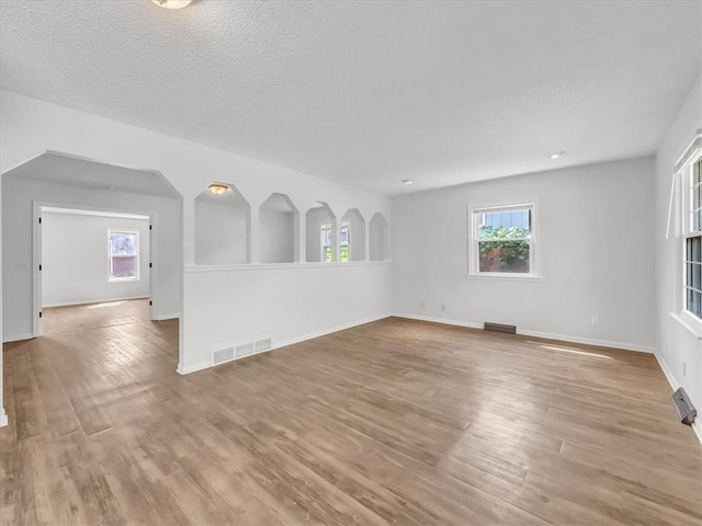 unfurnished living room with wood finished floors, visible vents, and baseboards