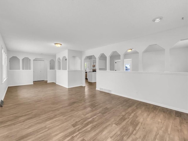 unfurnished living room with arched walkways, wood finished floors, visible vents, and baseboards