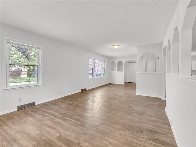 unfurnished living room featuring baseboards, wood finished floors, a textured ceiling, and visible vents
