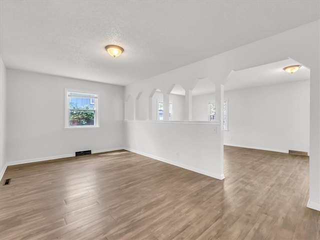unfurnished room featuring baseboards, visible vents, wood finished floors, and a textured ceiling