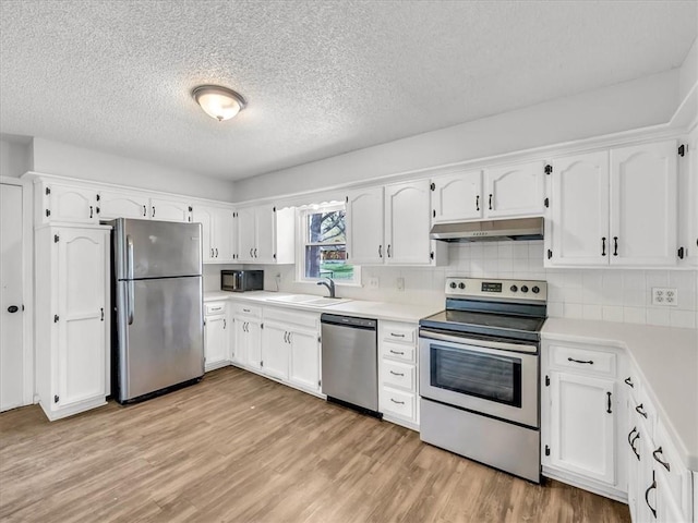 kitchen featuring white cabinets, under cabinet range hood, a sink, light wood-type flooring, and appliances with stainless steel finishes