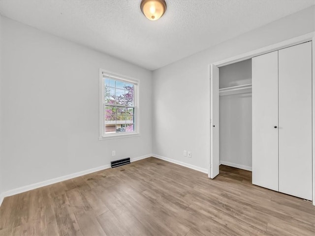 unfurnished bedroom with a textured ceiling, wood finished floors, visible vents, and a closet