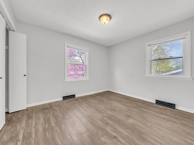 unfurnished bedroom with a textured ceiling, wood finished floors, visible vents, and multiple windows