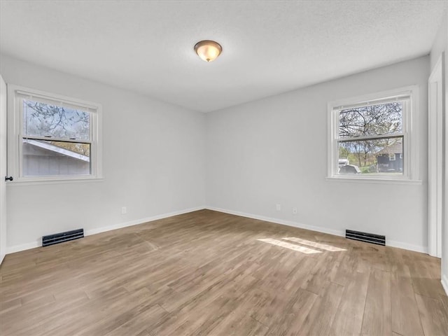 spare room with baseboards, wood finished floors, visible vents, and a textured ceiling
