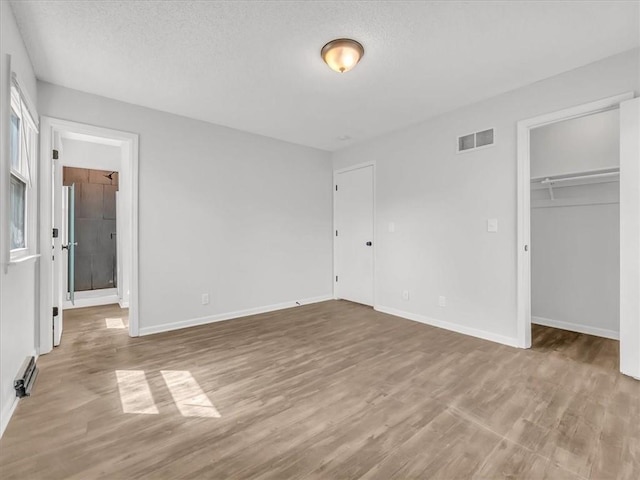 unfurnished bedroom with a textured ceiling, visible vents, baseboards, a spacious closet, and wood finished floors