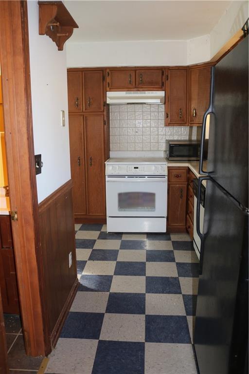 kitchen featuring white electric range oven, dark floors, stainless steel microwave, under cabinet range hood, and freestanding refrigerator