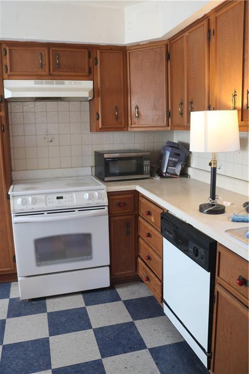 kitchen with light floors, under cabinet range hood, white appliances, and light countertops