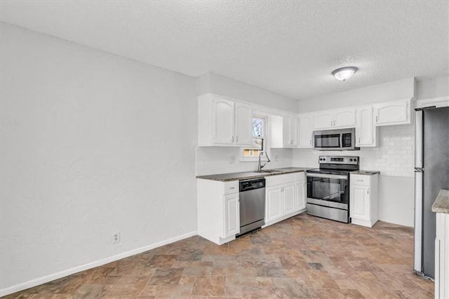 kitchen featuring white cabinets, stainless steel appliances, stone finish floor, a sink, and a textured ceiling