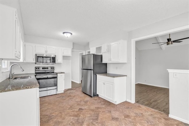 kitchen with dark stone counters, white cabinets, stainless steel appliances, and a sink