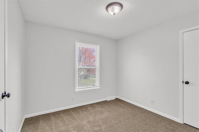 spare room featuring baseboards, dark carpet, and a textured ceiling