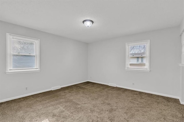 spare room featuring visible vents, baseboards, dark carpet, and a textured ceiling