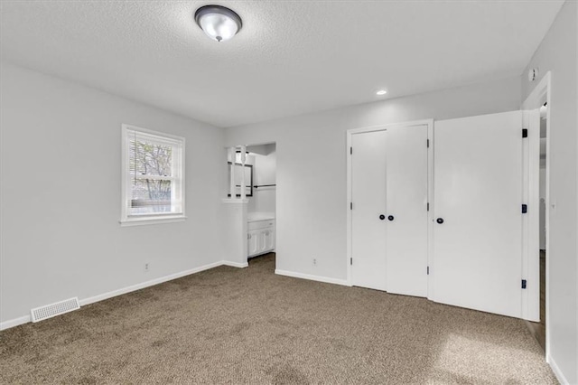 unfurnished bedroom with a textured ceiling, baseboards, visible vents, carpet floors, and connected bathroom