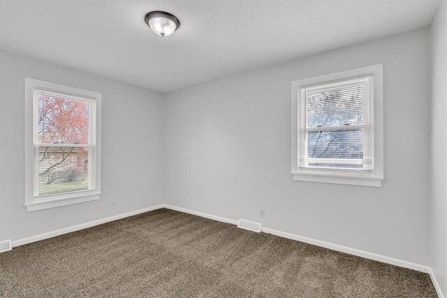 spare room with dark carpet, plenty of natural light, and visible vents