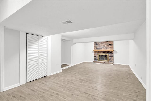 unfurnished living room with a brick fireplace, wood finished floors, visible vents, and baseboards