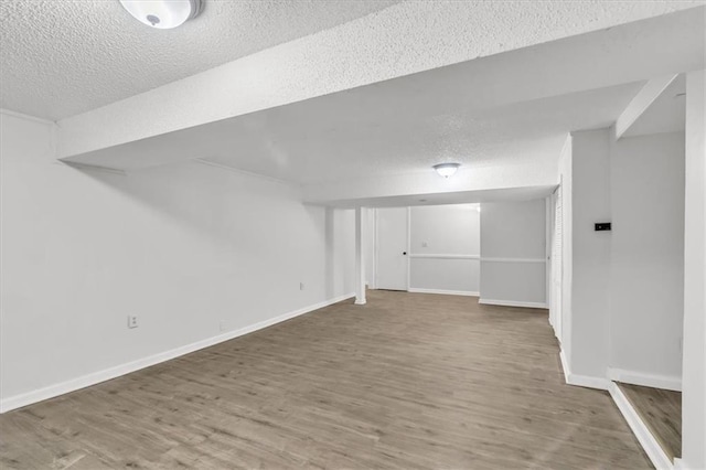 finished below grade area featuring baseboards, wood finished floors, and a textured ceiling
