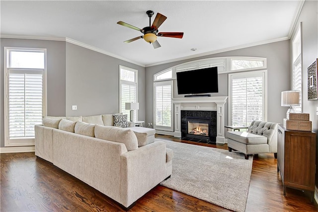 living area featuring crown molding, baseboards, dark wood-style floors, a tile fireplace, and a ceiling fan