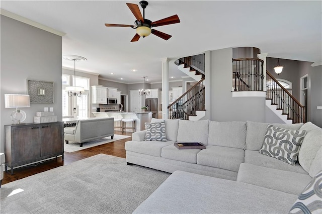 living room with dark wood-type flooring, ornamental molding, ceiling fan with notable chandelier, and stairway