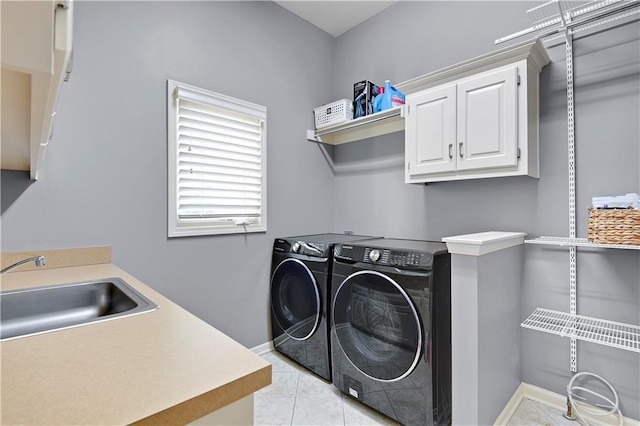 laundry room featuring baseboards, washing machine and clothes dryer, a sink, cabinet space, and light tile patterned floors