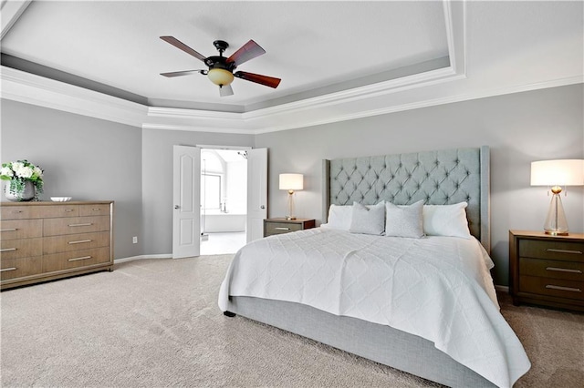 carpeted bedroom featuring a ceiling fan, baseboards, ensuite bathroom, a tray ceiling, and ornamental molding