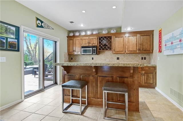 kitchen featuring decorative backsplash, stainless steel microwave, brown cabinets, and a kitchen bar