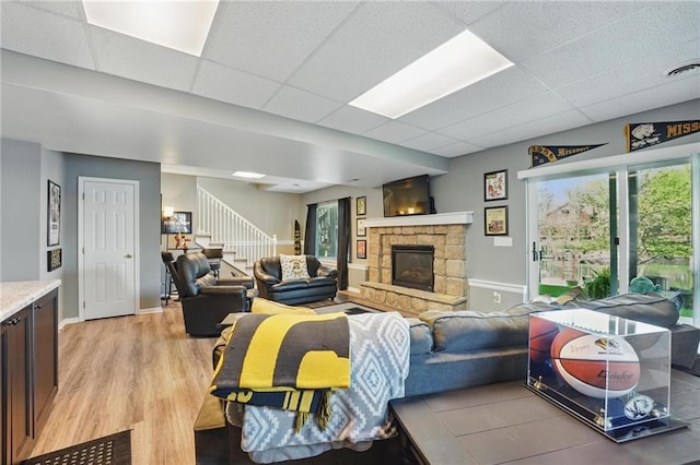 62 Beach Dr, Lake Tapawingo, MO 64015 - living room with light wood-style flooring, stairs, a stone fireplace, a drop ceiling, and baseboards