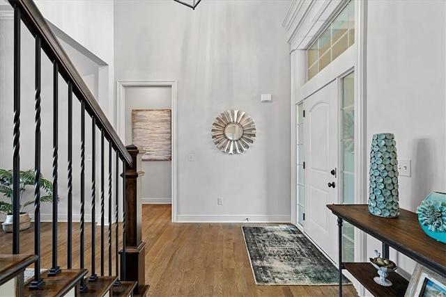 foyer entrance with baseboards, wood finished floors, stairway, and a towering ceiling