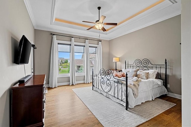 bedroom with a ceiling fan, wood finished floors, a raised ceiling, baseboards, and ornamental molding