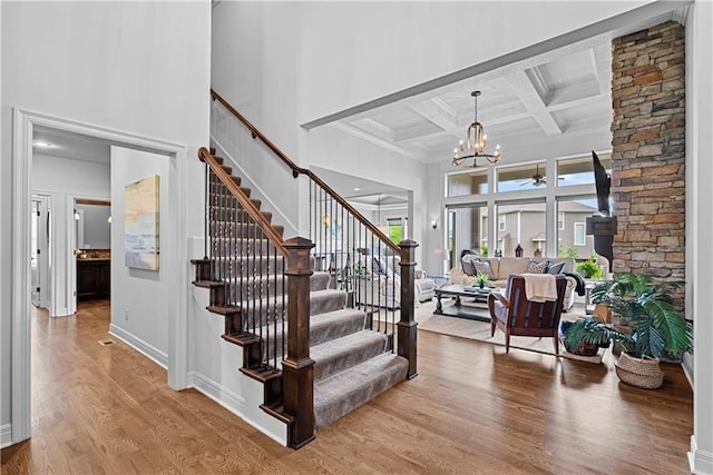 stairway with a high ceiling, beam ceiling, a chandelier, wood finished floors, and coffered ceiling