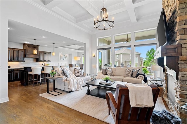 living room with a towering ceiling, wood finished floors, beamed ceiling, an inviting chandelier, and ornamental molding