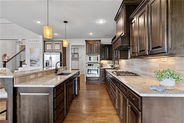 kitchen with dark brown cabinetry, a sink, stainless steel appliances, wood finished floors, and backsplash