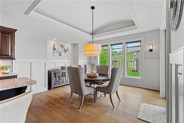 dining room with crown molding, a wainscoted wall, a decorative wall, and wood finished floors