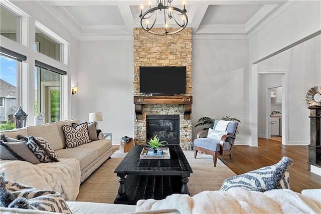 living room with a towering ceiling, a chandelier, a stone fireplace, and coffered ceiling