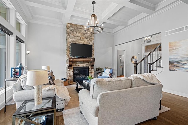 living area with a chandelier, a stone fireplace, beamed ceiling, visible vents, and stairway