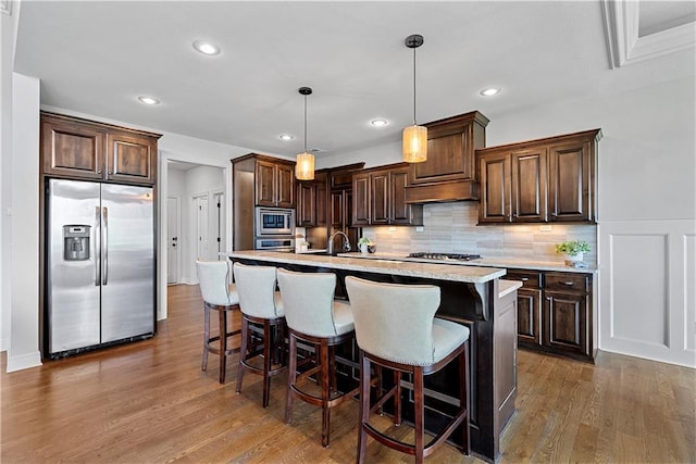 kitchen with a kitchen breakfast bar, dark brown cabinetry, appliances with stainless steel finishes, and dark wood-type flooring
