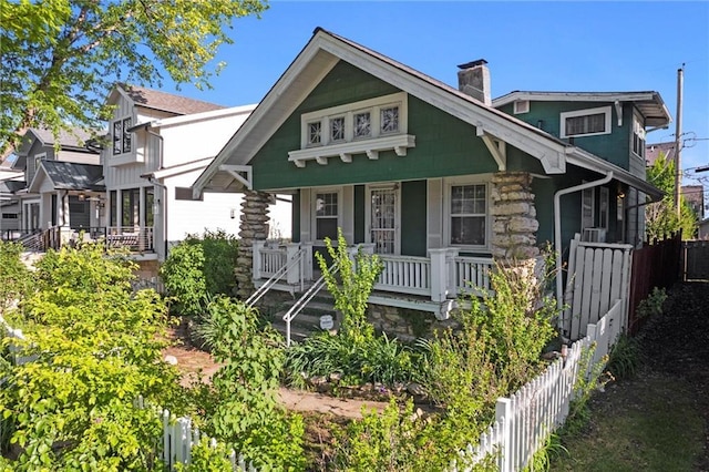 bungalow-style home featuring fence, covered porch, a chimney, and stone siding