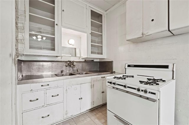 kitchen with white gas range oven, a sink, light countertops, white cabinetry, and glass insert cabinets