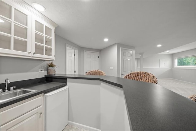 kitchen featuring carpet floors, dark countertops, glass insert cabinets, white cabinets, and a sink
