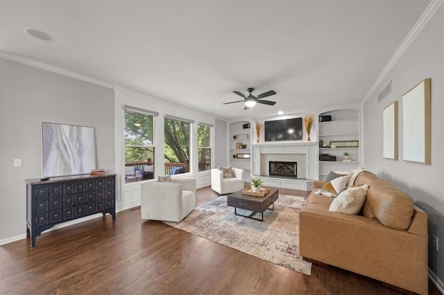 living area featuring crown molding, a fireplace with raised hearth, built in features, wood finished floors, and visible vents